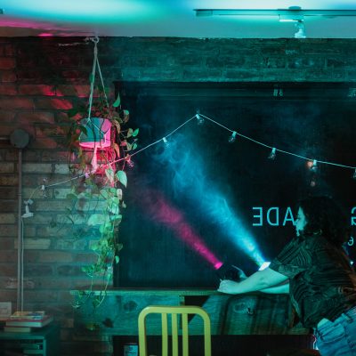 OtM Director of Production Tori Morrison adjusts the beams of a blue and pink stage light inside a cafe.